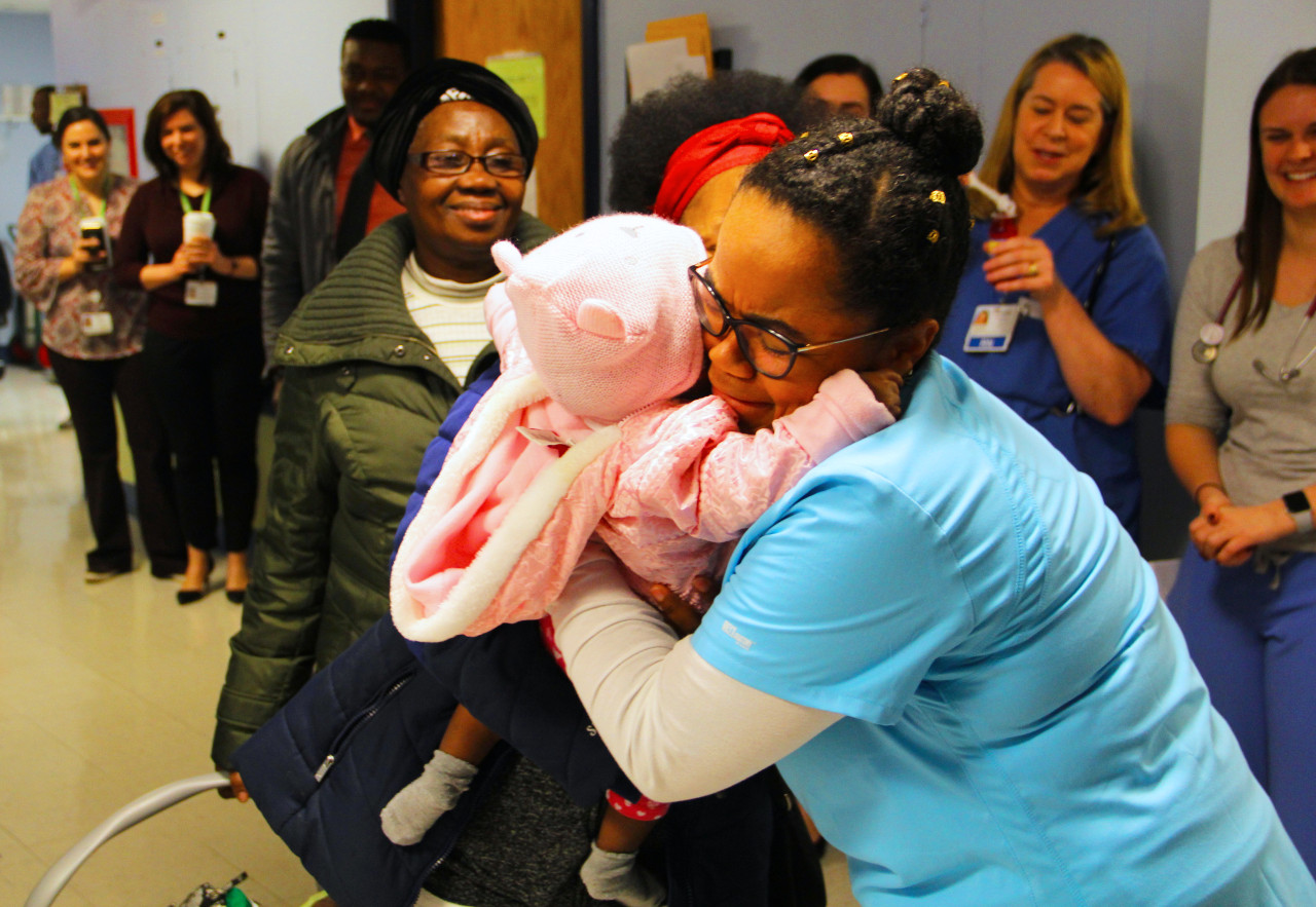 a nurse hugging a young girl while a group of people watch
