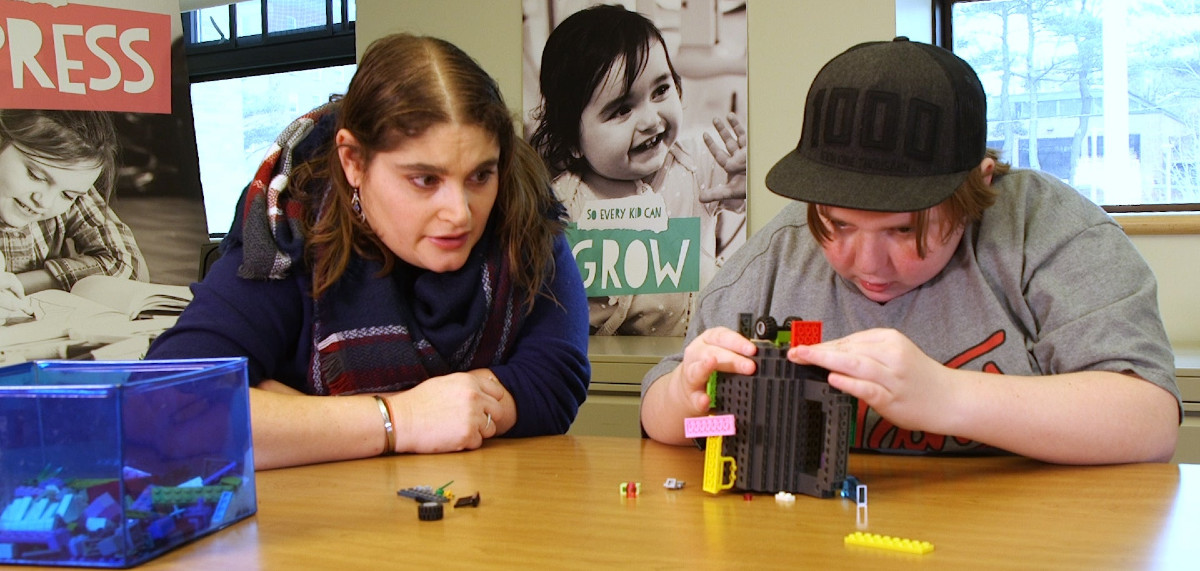 a boy playing with legos while a woman watches over him