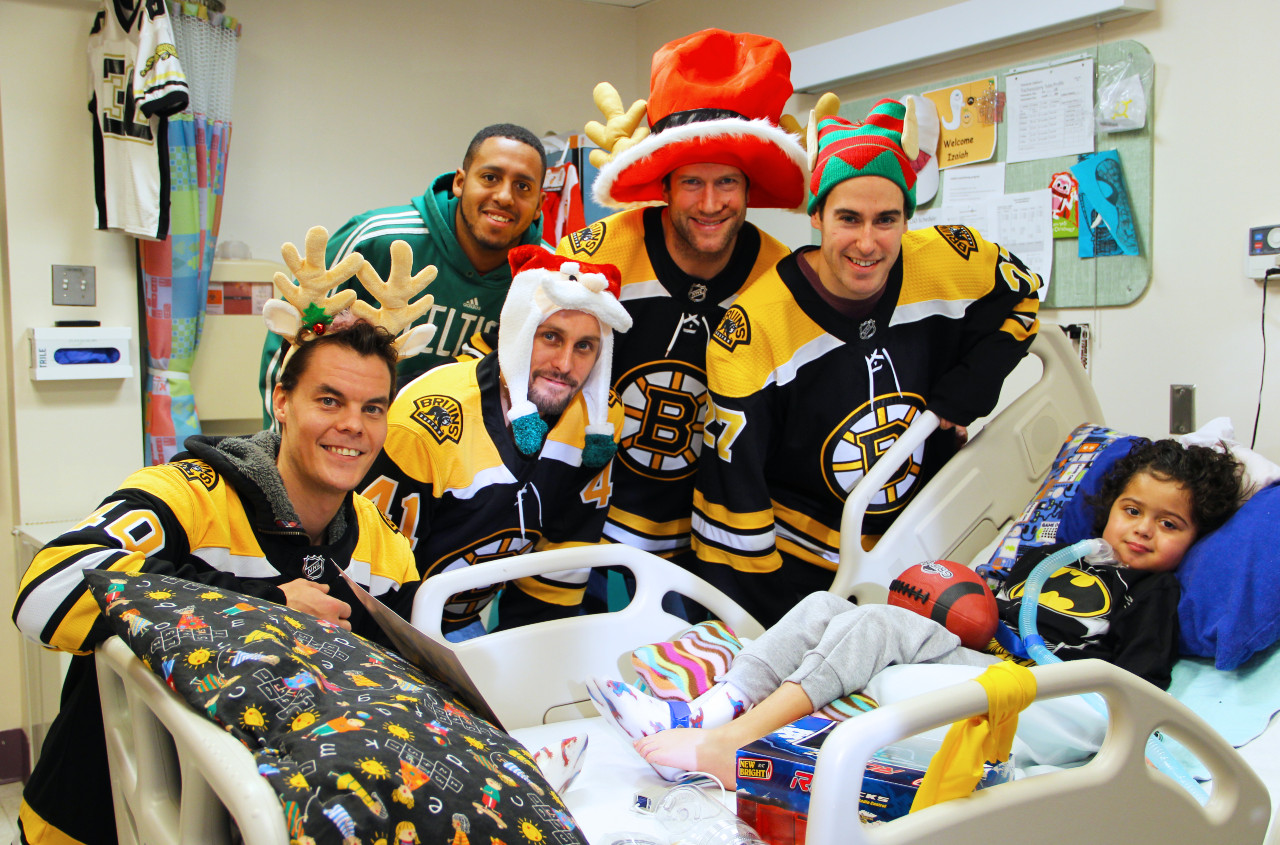a group of boston bruins players arounding a boy in a hospital bed