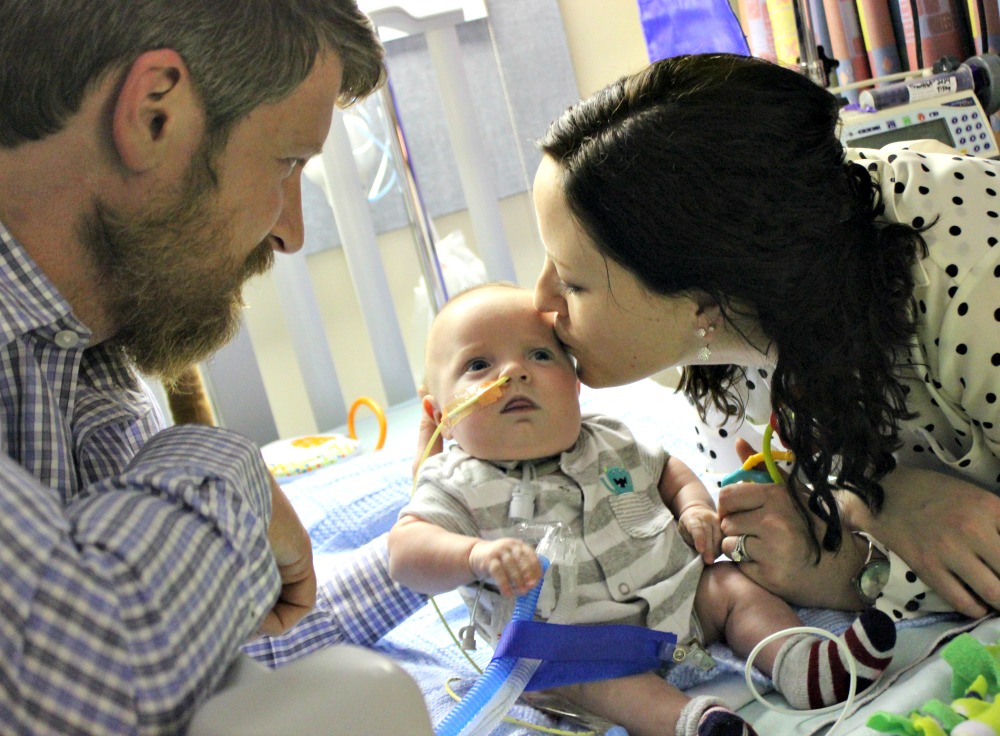 a mother kissing a baby while a father looks on