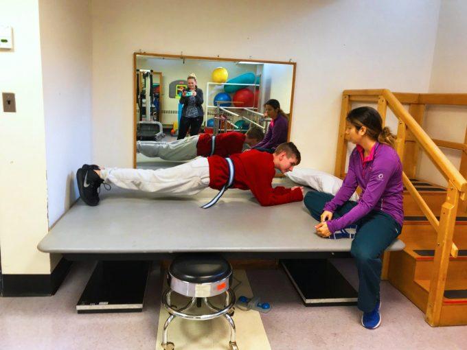 a boy doing a plank on a therapy table while a woman watches