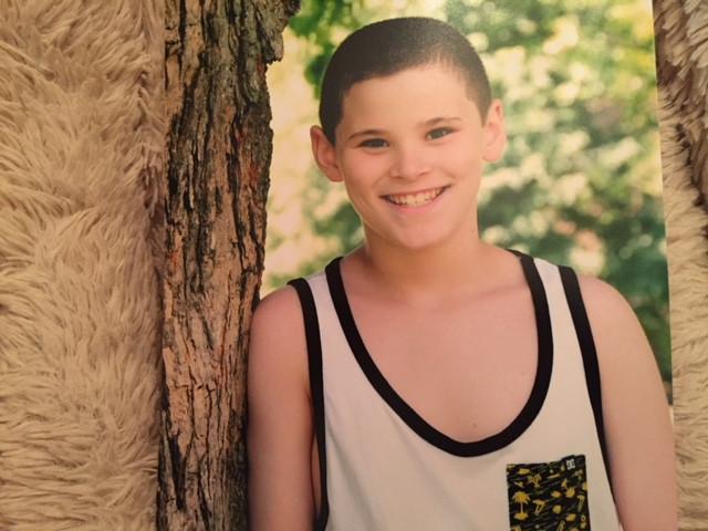 a smiling teen boy leaning against a tree