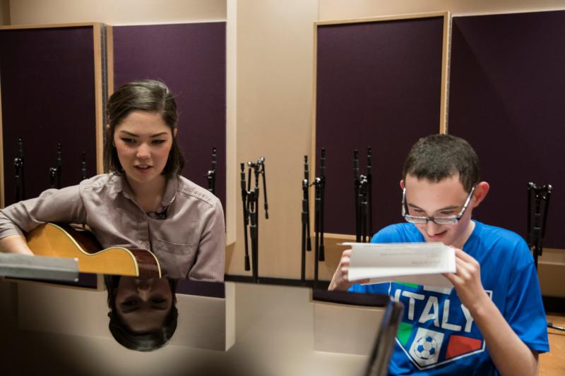 a boy reading music as his teacher plays the guitar